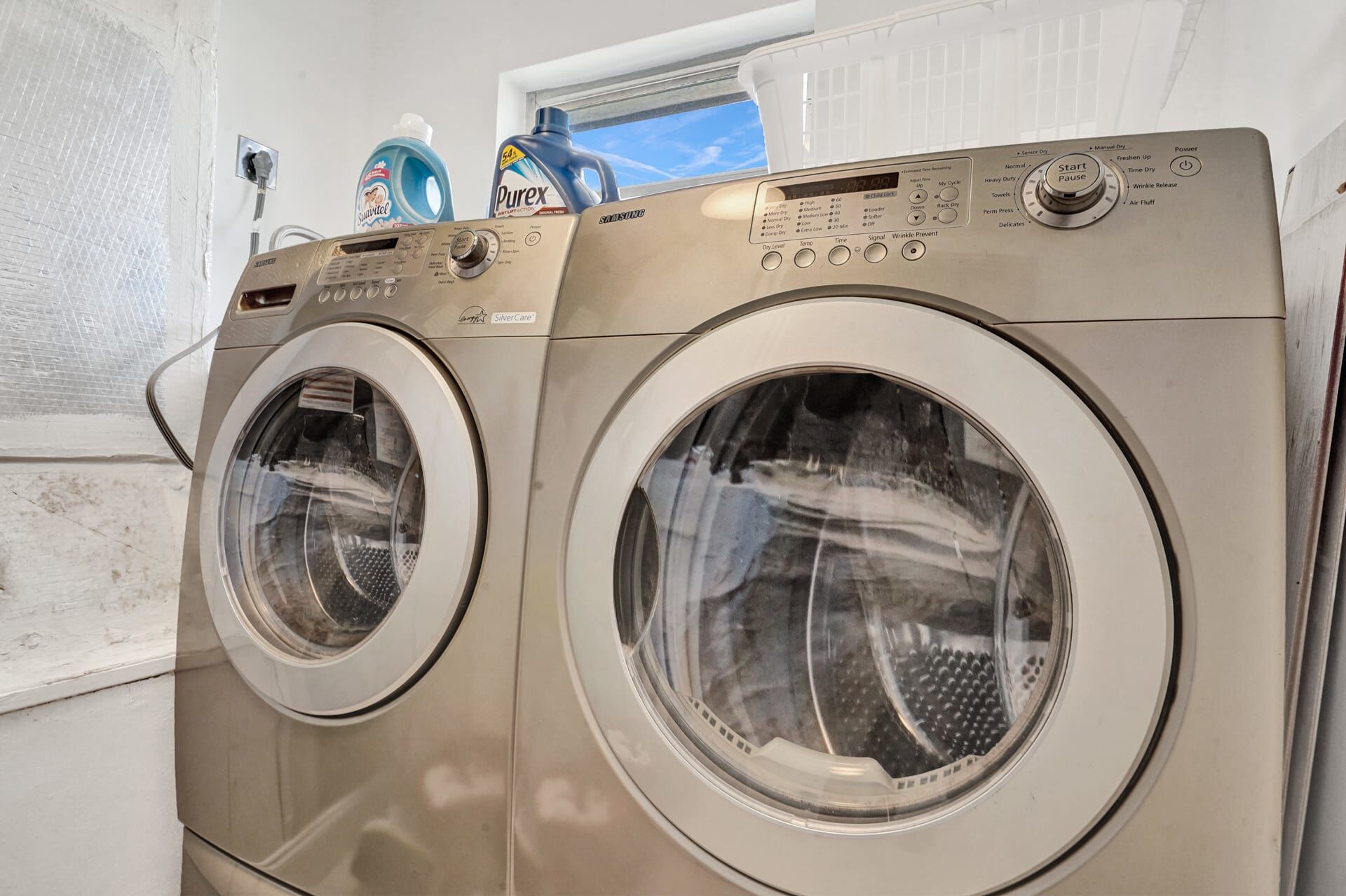 Two front-loading stainless steel washers with a control panel, a window above, and a detergent bottle on the wall.