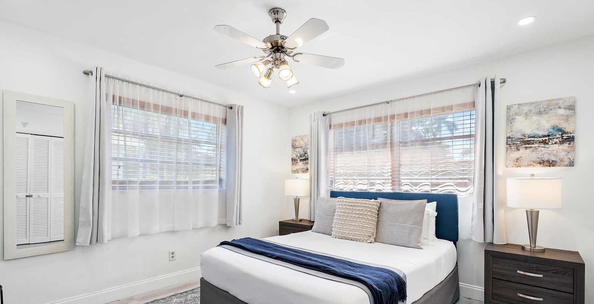A bedroom with a bed, two bedside tables, a ceiling fan, and a window with curtains.