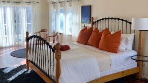 A bedroom with a wooden bed, white bedding, orange pillows, a black metal headboard, a ceiling fan, and a view of the outdoors through large windows. - Wild Horse Country Stay • Mt. Rose Views Near Reno (Reno)
