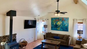 A living room with a stone fireplace, a ceiling fan, a large abstract painting, and a television on the wall. - Wild Horse Country Stay • Mt. Rose Views Near Reno (Reno)