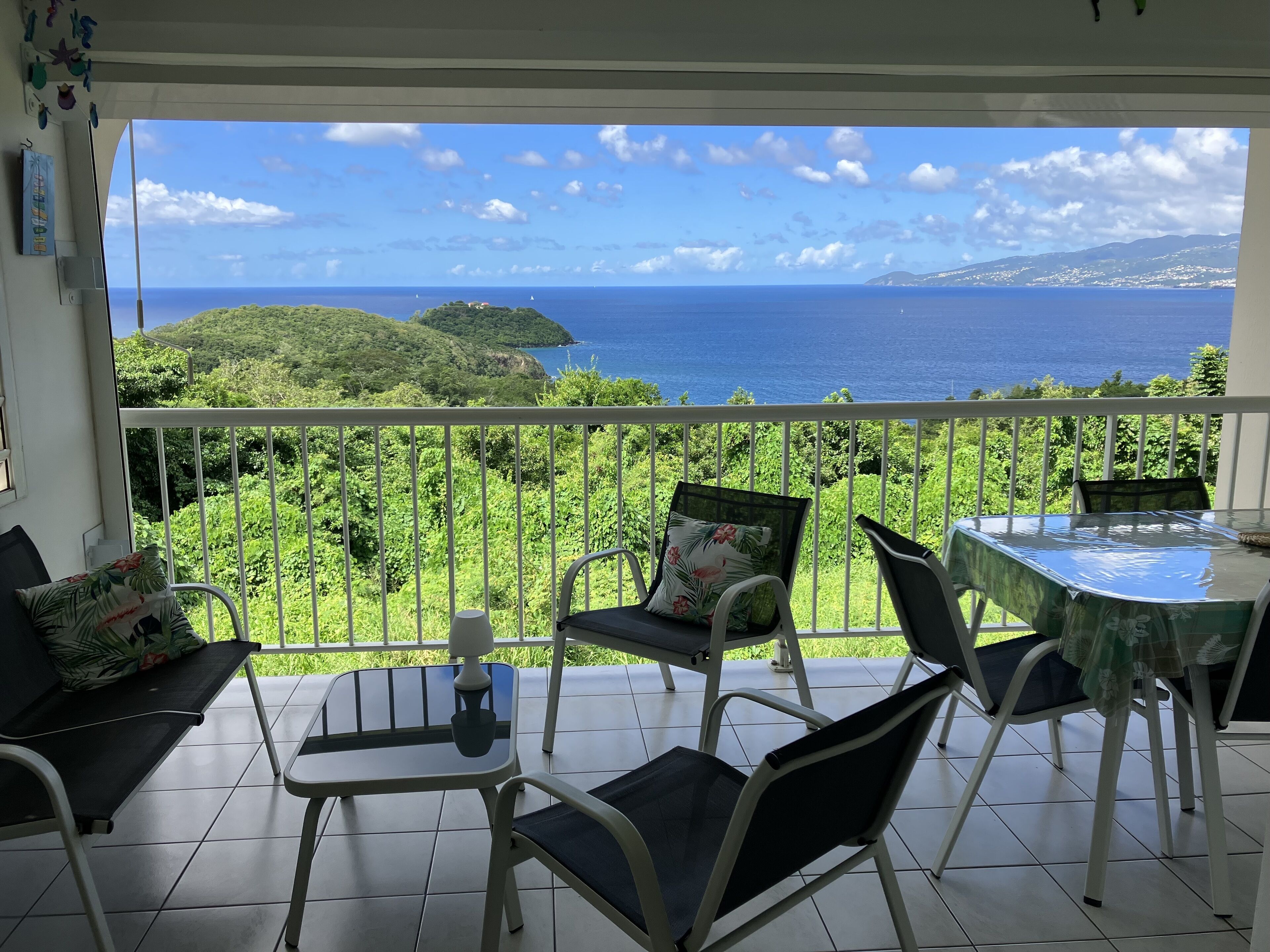 Un balcon avec vue sur la mer et les collines, aménagé avec des chaises et une table.