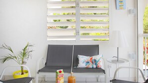 A modern outdoor seating area with a glass table, two chairs, a sofa with a colorful pillow, a potted plant, and a bottle of drink. - L'Oiseau Bleu - 1bed - 4p - Sea view - Beach 600m (Les Trois-Îlets)