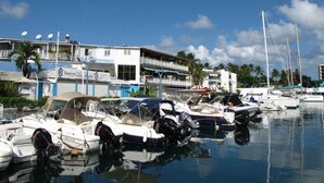 A marina with several boats docked, a building with a sign that reads "Restaurant of the Beach," and a clear blue sky. - L'Oiseau Bleu - 1bed - 4p - Sea view - Beach 600m (Les Trois-Îlets)