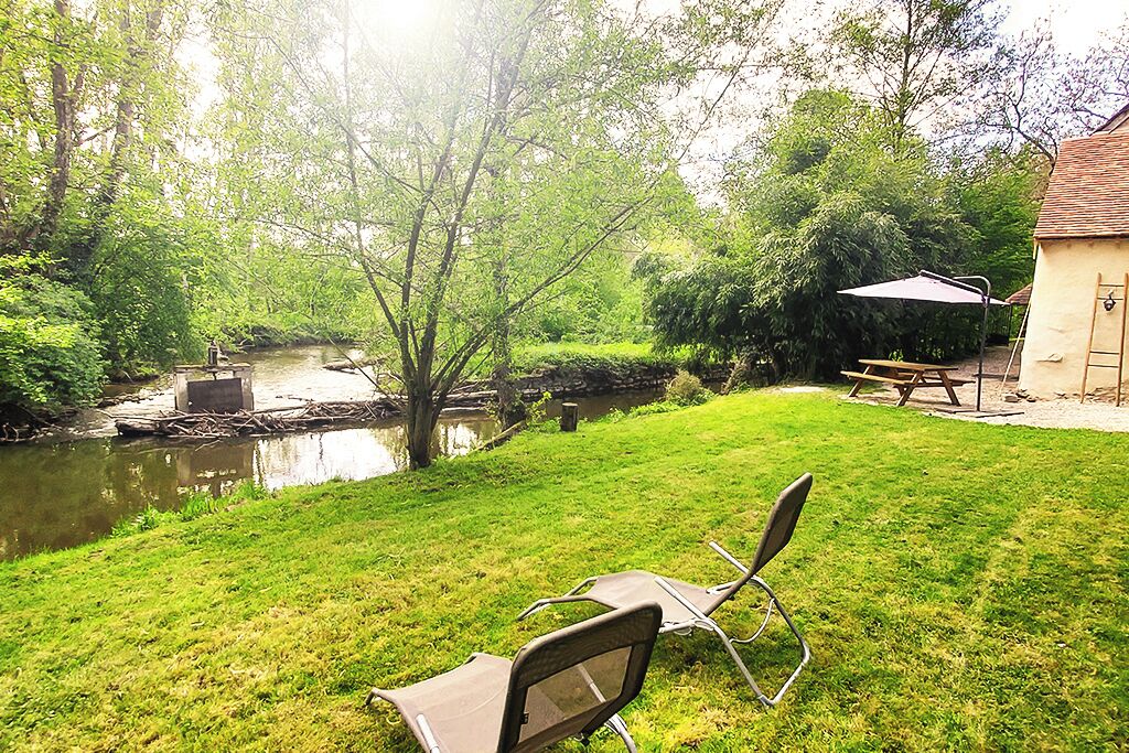 A grassy backyard with a picnic table and chairs, a small pond, and a house with a tiled roof.