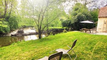 A grassy backyard with a picnic table and chairs, a small pond, and a house with a tiled roof.