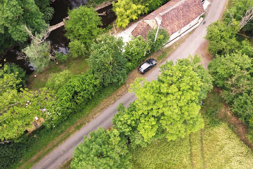 Une vue aérienne d’une route où l’on aperçoit une voiture, entourée d’une végétation luxuriante et d’un bâtiment doté d’un toit en tuiles.