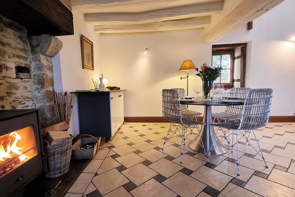 Una stanza accogliente con un camino in pietra, un tavolo da pranzo con sedie in metallo, una lampada e un vaso con fiori.