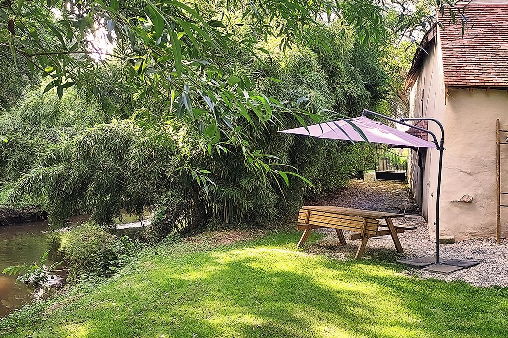 A wooden bench under a purple umbrella, a small pond, and dense greenery.
