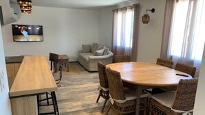 Una sala de estar moderna con una mesa de comedor de madera, sillas de mimbre, un sofá y un televisor montado en la pared.