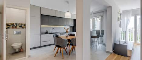 A modern kitchen with grey cabinets, a dining area with a round table and chairs, and a view of the city through large windows.