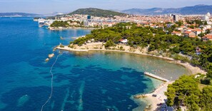 A coastal town with a beach, clear blue waters, and a mix of residential and commercial buildings. - Modern 90 m2 apt With Balcony w the sea View (Split)