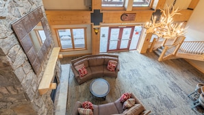 A spacious loft-style room with a stone wall, a large wooden ceiling, and a fireplace. There is a curved brown sofa with red pillows and a round coffee table in the center. - Perfect views of the Super Bee Lift, Free WiFi, underground parking (Copper Mountain)