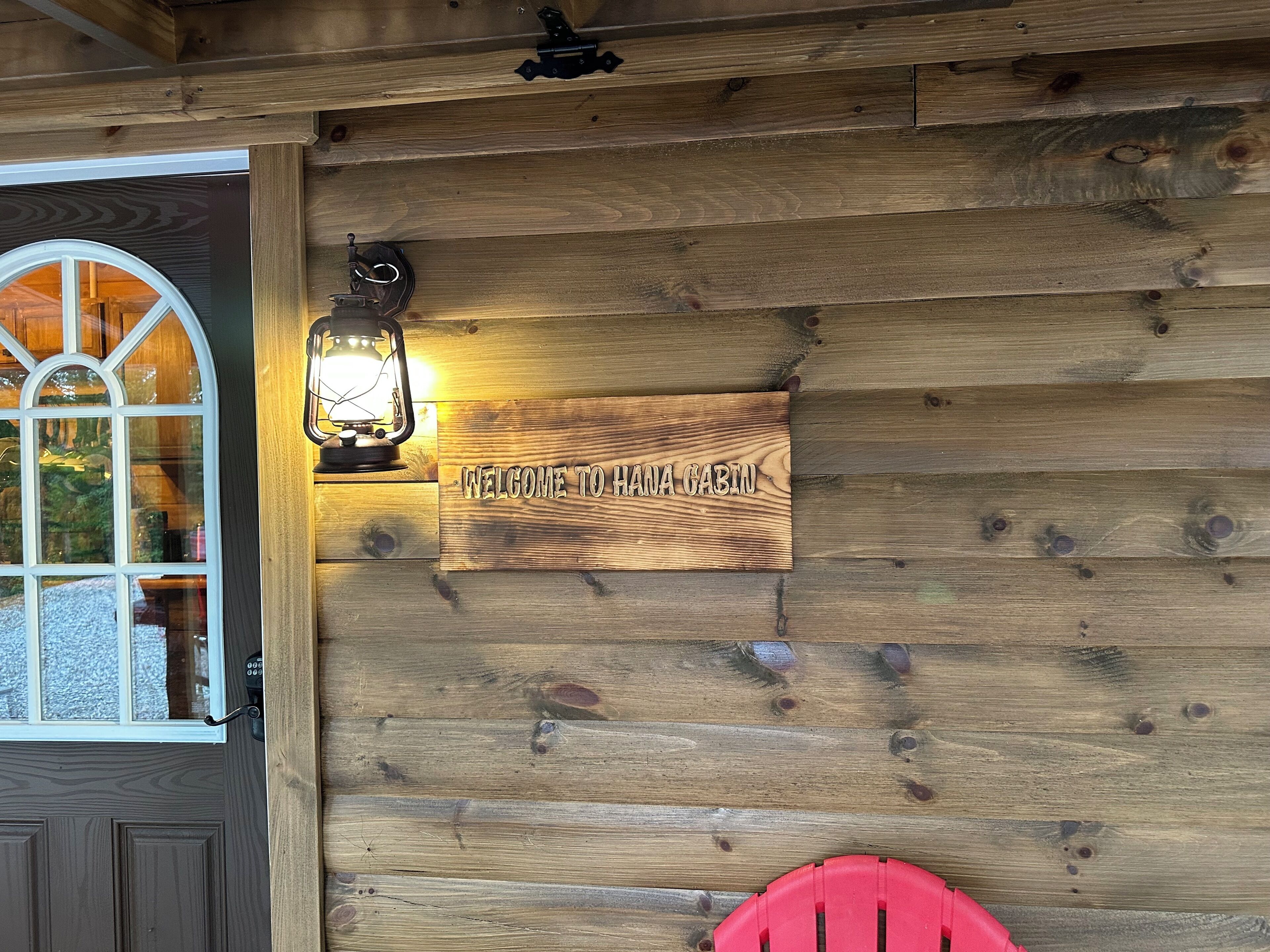 Une cabane en bois avec une pancarte indiquant « Bienvenue », une lanterne et une chaise rouge.