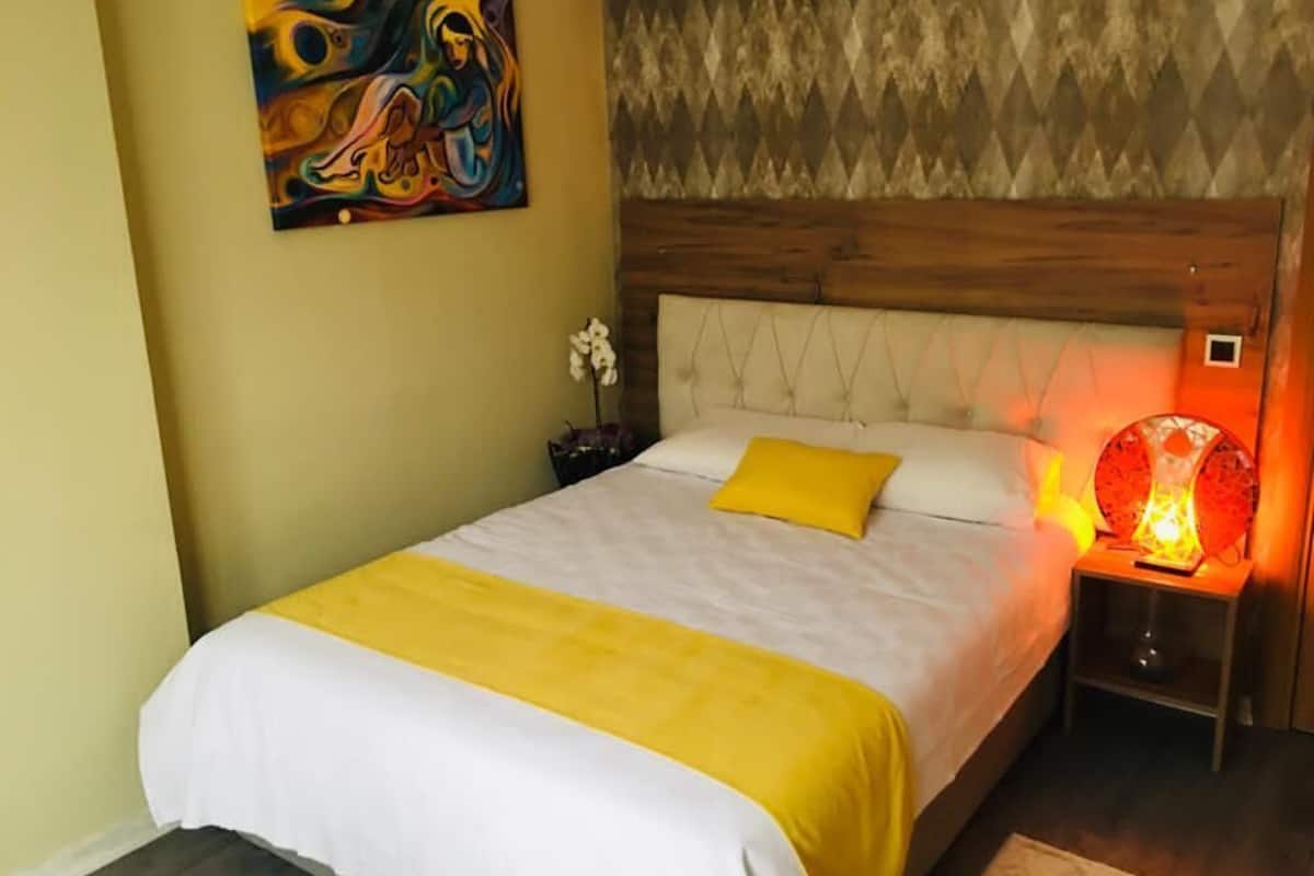 A bedroom with a bed, a nightstand, a lamp, and a painting on the wall.