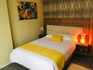 A bedroom with a bed, a nightstand, a lamp, and a painting on the wall. - RİSE SUİT OTEL (Sarikaya)