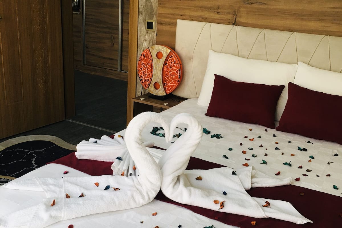 A hotel room with a bed, a wooden headboard, a nightstand with a decorative item, and a door.