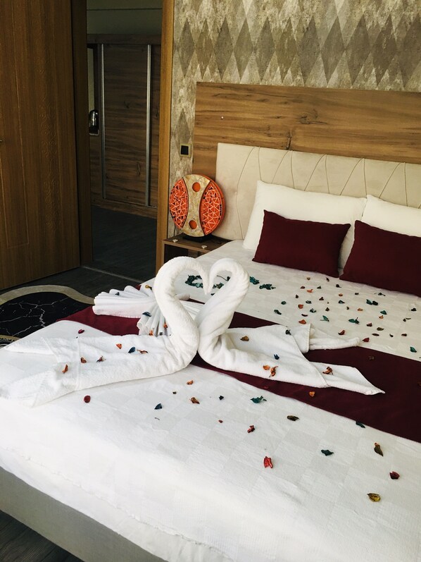 A hotel room with a bed, a wooden headboard, a nightstand with a decorative item, and a door. - RİSE SUİT OTEL (Sarikaya)
