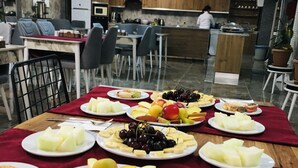 A dining area with a table set for a meal, featuring various fruits and desserts. - RİSE SUİT OTEL (Sarikaya)