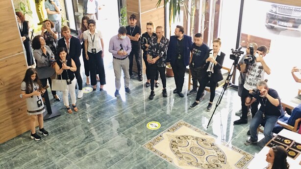 A group of people in a lobby with a marble floor, a wooden reception desk, and a large window. - RİSE SUİT OTEL (Sarikaya)