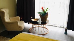 A hotel room with a bed, a chair, a small round table with a plant, and a window with curtains. - RİSE SUİT OTEL (Sarikaya)