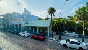 A street view with parked cars, a building with a green roof, and palm trees.