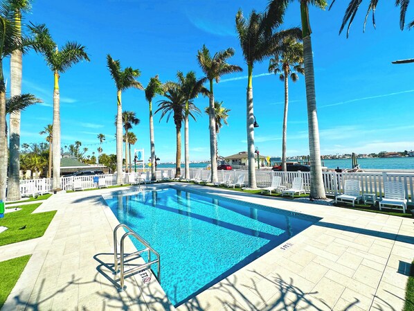 A swimming pool with a white fence, palm trees, and a view of the sea.