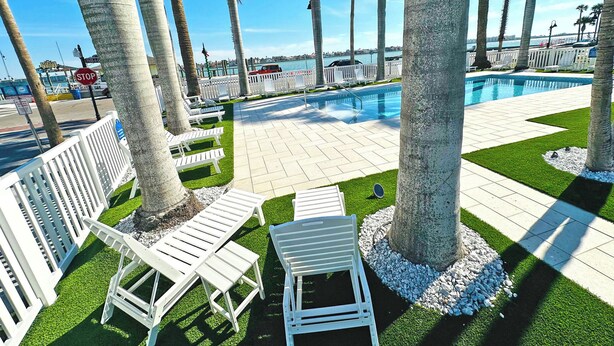 A poolside area with white lounge chairs, palm trees, and a view of the water.