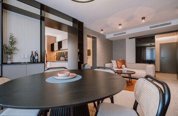 A modern living room with a round dining table, a sofa, and a kitchen area in the background.