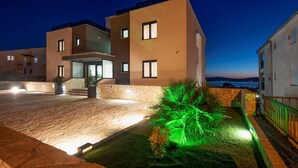 A modern hotel with a stone facade, a well-lit entrance, and a view of the sea. - Villa Ivan pool apartament (Sv. Filip I Jakov)