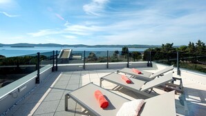 A rooftop terrace with sun loungers, a glass balustrade, and a view of the sea and hills. - Villa Ivan pool apartament (Sv. Filip I Jakov)