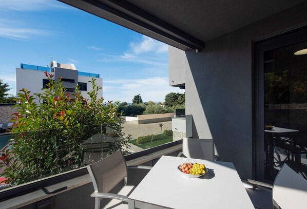 Un balcón con mesa y sillas, un frutero y vistas a edificios y vegetación.