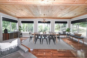 Un espace repas doté d’un plafond en bois, de grandes fenêtres et d’un lustre.