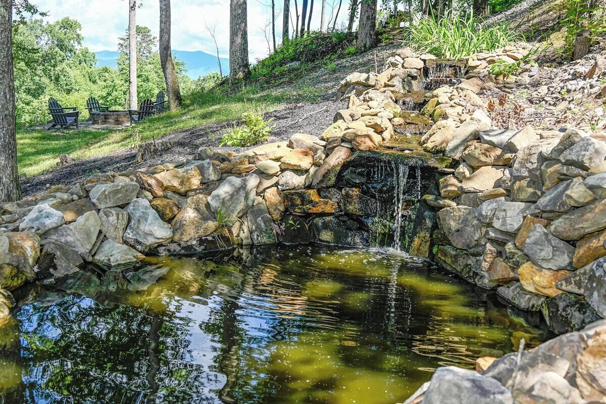 A natural stone waterfall, a small pond, and a seating area with chairs.