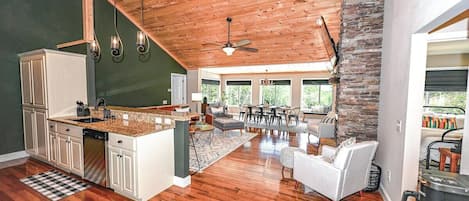 A spacious kitchen with wooden flooring, a dining area with a large window, and a living room with a fireplace.