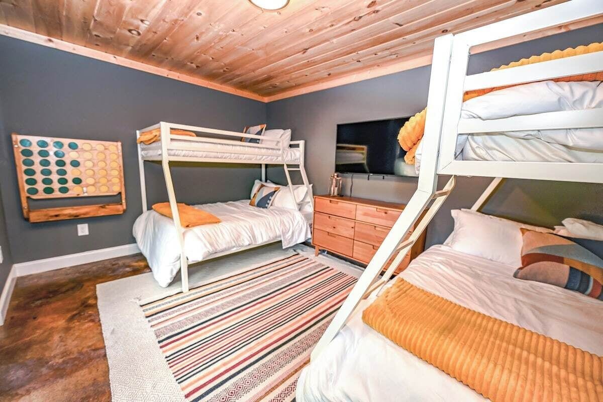 A room with bunk beds, a wooden ceiling, a patterned rug, and a wall-mounted board game.