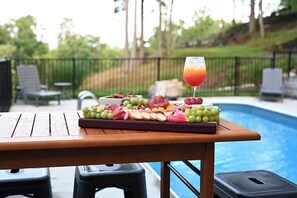 A poolside table with a charcuterie board and a glass of orange juice.
