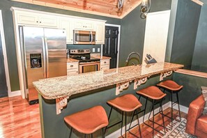 A kitchen with a granite countertop, stainless steel appliances, and a bar area with stools. - Barefoot in the Blue Ridge (Hayesville)