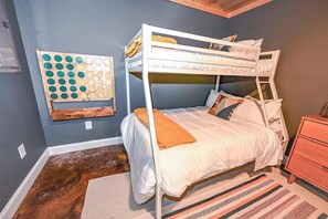 Une chambre avec des lits superposés, un jeu de société en bois accroché au mur, un tapis à motifs et une table de chevet en bois.