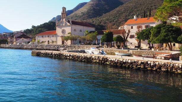 Eine Küstenstadt mit einer markanten Kirche, Steinhäusern und einem Steg, der sich ins Wasser erstreckt.