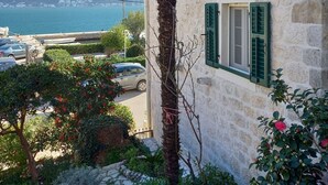 Ein Steinhaus mit grünen Fensterläden, Blick auf das Meer und eine gebirgige Landschaft im Hintergrund.