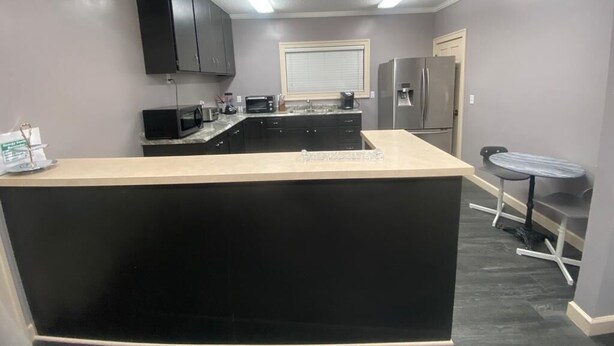 A modern kitchen with a central island, black cabinets, a refrigerator, and a microwave.
