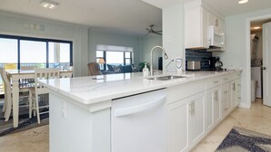 Eine moderne Küche mit weißen Schränken, einer großen Kochinsel mit Spüle und einem Essbereich mit Tisch und Stühlen.