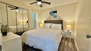 A bedroom with a bed, bedside lamps, a ceiling fan, a large mirror, and a potted plant. - Grand Deluxe Garden 3BR Penthouse near Disney Parks (Kissimmee)