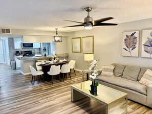 A modern living room with a glass coffee table, a sofa, and a dining area with chairs and a table set for tea.
