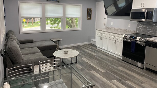A modern kitchen with white cabinets, a stainless steel oven, and a microwave. There is a gray sofa and a glass coffee table in the living area. - North Shore Loft, close to everything! (Clear Lake)