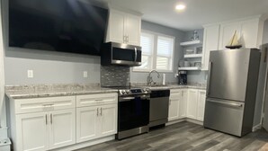 A modern kitchen with white cabinets, stainless steel appliances, a large flat-screen TV, and a wooden floor. - North Shore Loft, close to everything! (Clear Lake)