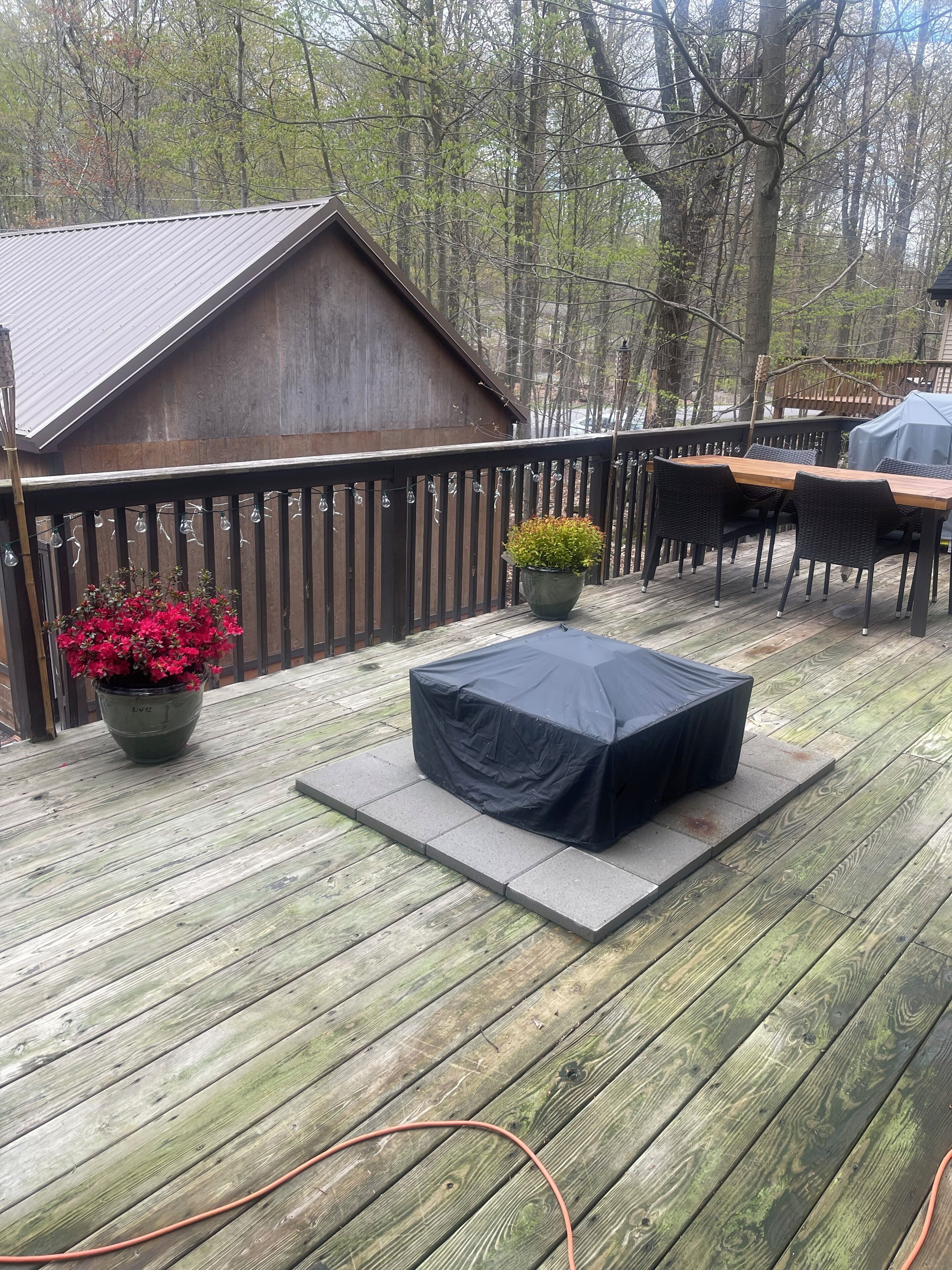 Une terrasse en bois avec une table couverte, des chaises et un pot de fleurs.