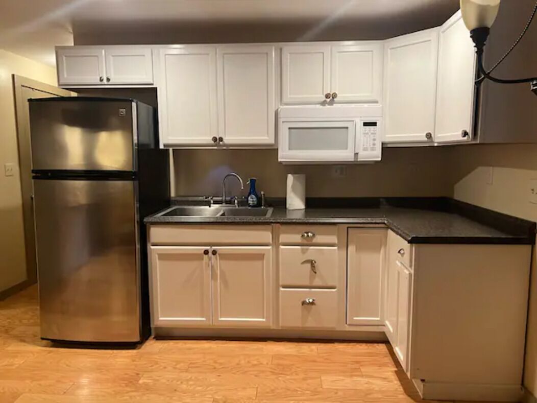 A kitchen with white cabinets, a stainless steel refrigerator, a microwave, and a sink.