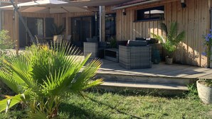A wooden house with a patio area, outdoor seating, and potted plants. - Agréable Maison Bois (Andernos-les-Bains)