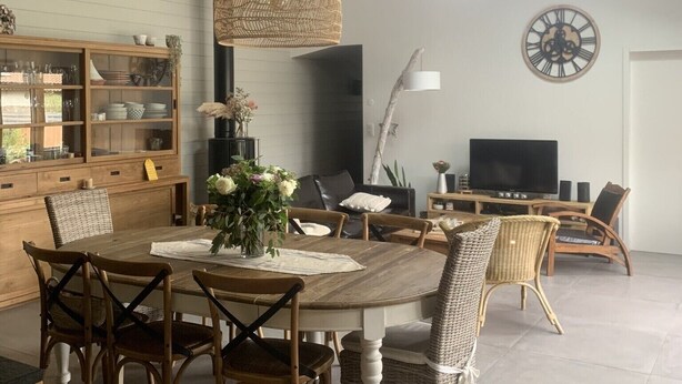 A spacious dining area with a wooden table, wicker chairs, and a hanging light fixture. - Agréable Maison Bois (Andernos-les-Bains)